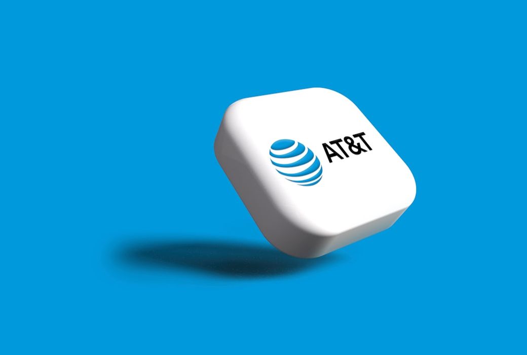 An AT&T logo displayed on a stylized 3D cube against a bright blue background. The logo features the recognizable blue globe symbol along with the brand name 'AT&T'. — Credit: Photo by Rubaitul Azad on Unsplash