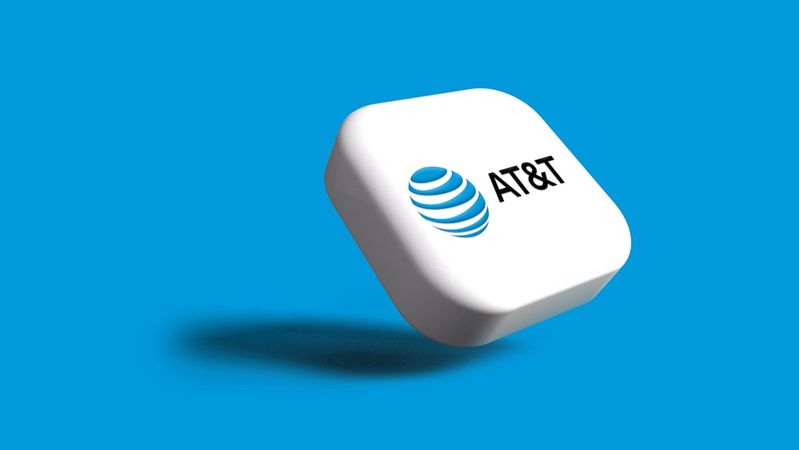 An AT&T logo displayed on a stylized 3D cube against a bright blue background. The logo features the recognizable blue globe symbol along with the brand name 'AT&T'.