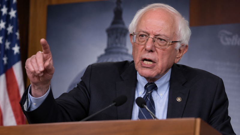 The image captures Bernie Sanders passionately addressing an audience, emphasizing his points with an intense expression and raised finger. Behind him is a backdrop featuring the U.S. Capitol, highlighting his political context.