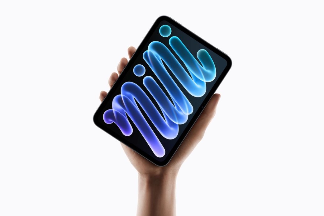The image features a person holding the new iPad Mini in one hand, showcasing the device's sleek design and vibrant screen. The display highlights the word 'mini' in a dynamic, colorful font, emphasizing its compactness and modern aesthetics.