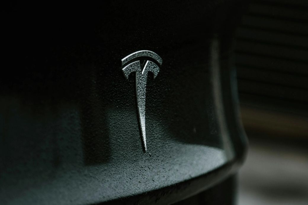 A close-up image of the Tesla logo displayed on a vehicle. The logo is sleek and modern, reflecting the brand's focus on innovation in the automotive industry. — Credit: Photo by Austin Ramsey / Unsplash