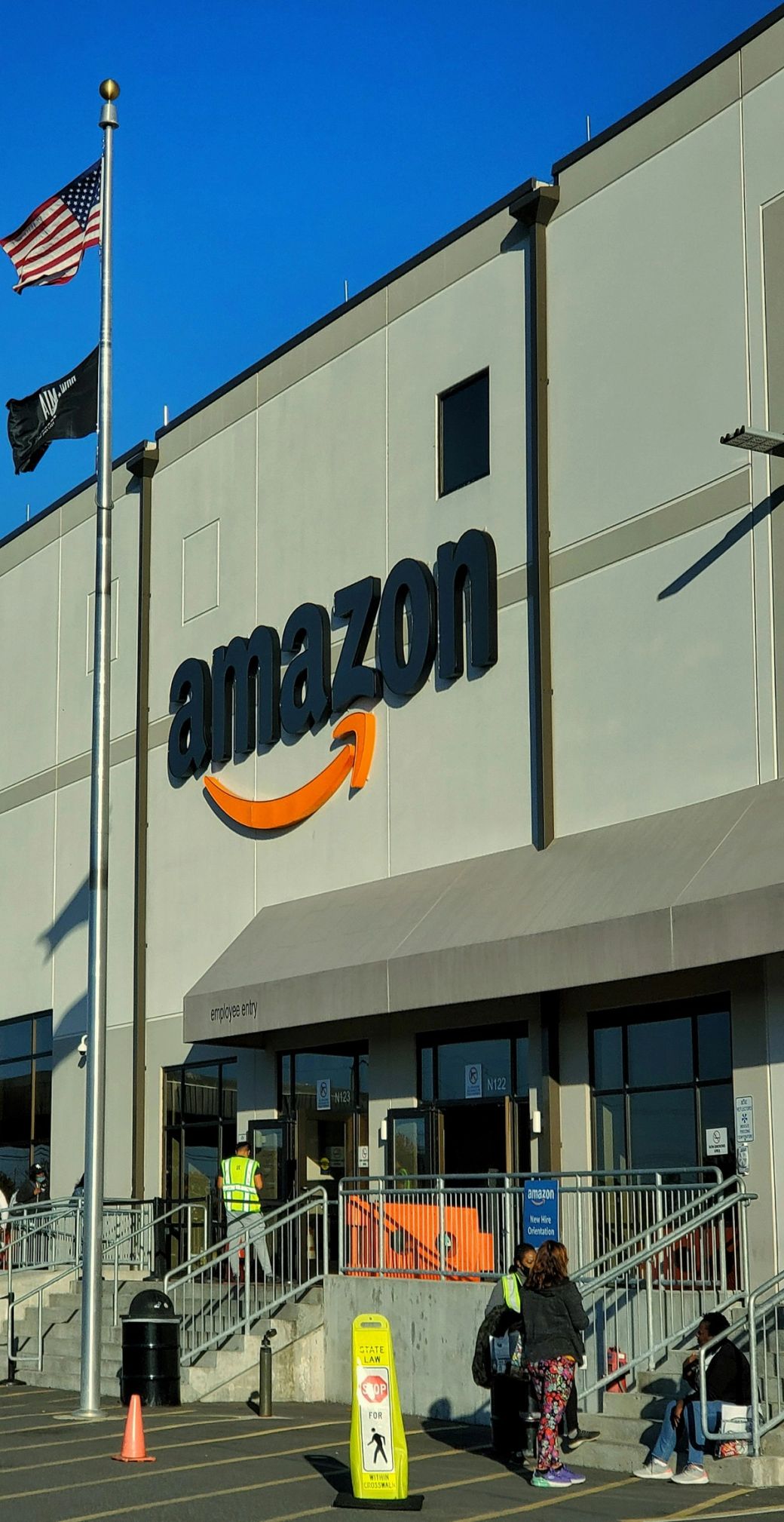 An exterior view of an Amazon warehouse with the company logo prominently displayed. The building is well-lit and showcases the recognizable branding of Amazon. — Credit: Photo by Yender Gonzalez / Unsplash