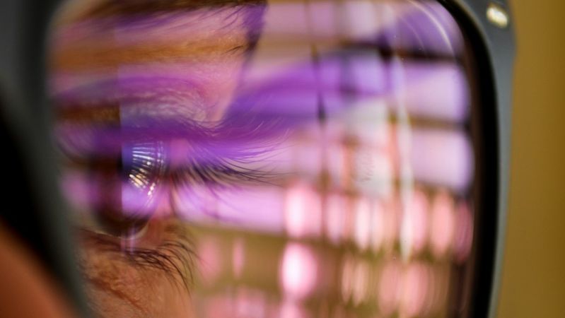 The image captures a close-up of a person's eye reflected in glasses, showcasing colorful light patterns and abstract visuals. The focus is on the intricate details of the eye and the vibrant reflections within the lenses.