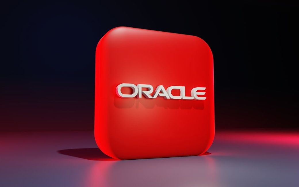 The image features a prominently displayed three-dimensional logo of Oracle, set against a gradient background. The logo is rendered in white text on a vibrant red square platform. — Credit: Photo by BoliviaInteligente on Unsplash