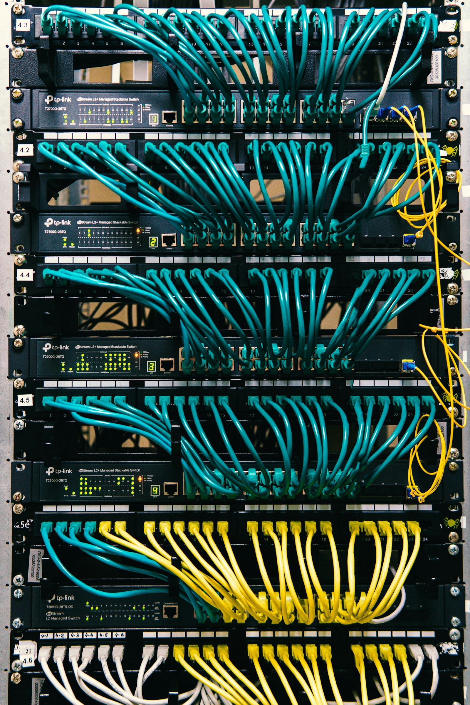 The image showcases a close-up view of network switches with numerous blue and yellow Ethernet cables connected. The equipment is part of a server rack, typically used in data centers or networking environments.