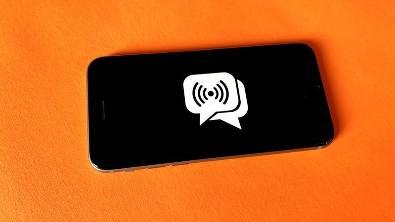 The image features a smartphone laying on a vibrant orange surface. The screen displays a speech bubble icon with sound waves, suggesting communication or audio transmission.