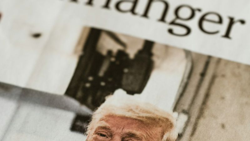 A close-up shot of a newspaper front page featuring a headline about a cliffhanger, with a prominent image of a man with light-colored hair. The newspaper is clearly identified as the New York Times, dated November 3.