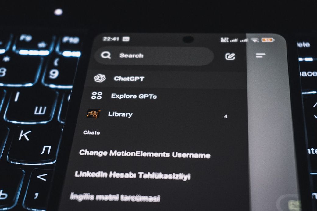 The image shows a close-up view of a smartphone screen with a dark user interface. The screen displays various options, including 'Search,' 'Explore GPTs,' and 'Library,' indicating a focus on AI and chat features. — Credit: Photo by Zulfugar Karimov on Unsplash