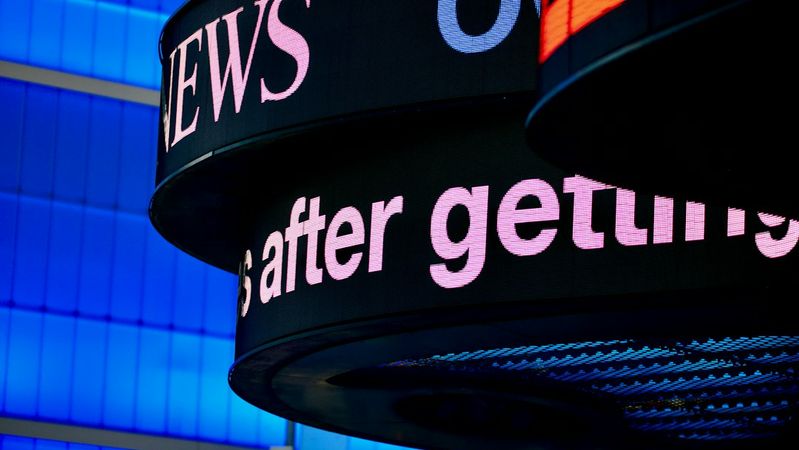 The image features a digital news ticker displaying text on a modern electronic panel with a vibrant blue background. The visible text suggests a news update, highlighting a significant event or development.