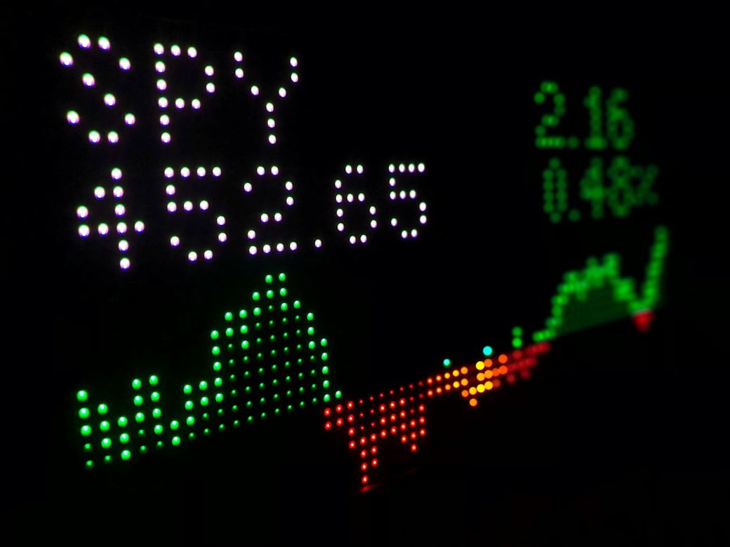 The image displays a digital stock market ticker showing the performance of the SPY ETF with a current price of 452.65 and a change of 2.16, represented by colorful lights. The background is dark, emphasizing the bright LED display. — Credit: Photo by Tyler Prahm on Unsplash