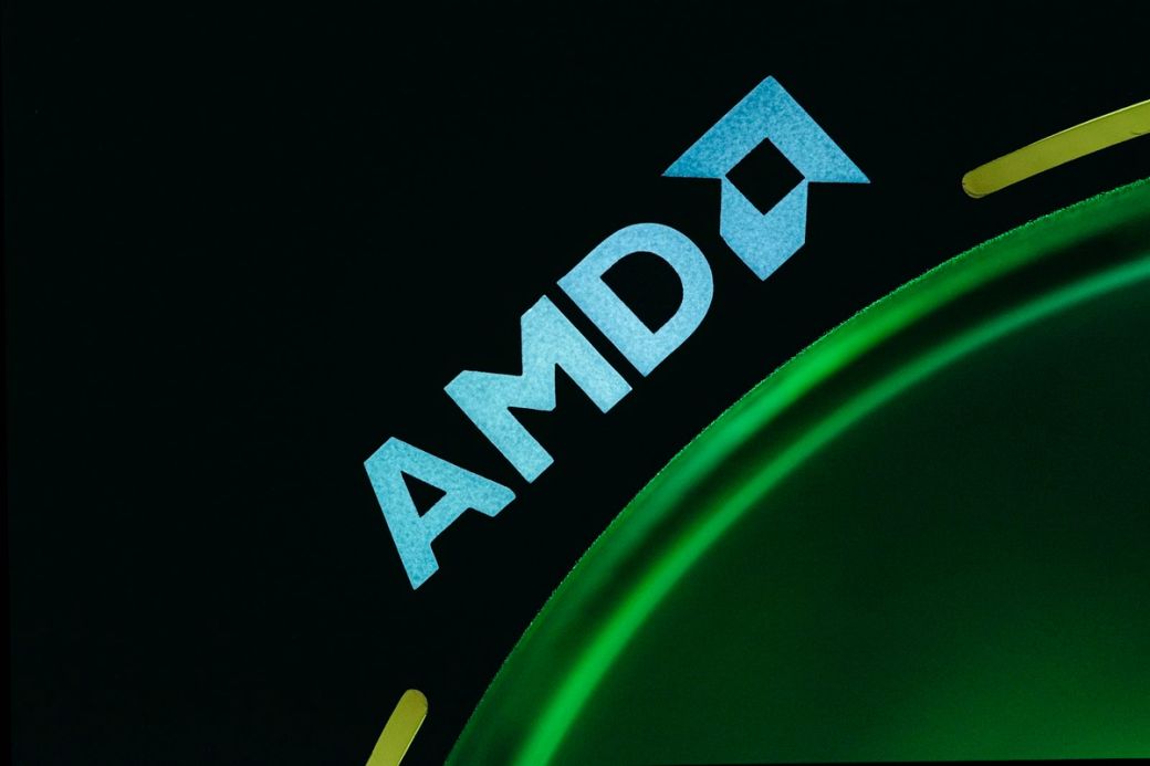 The image features a close-up of the AMD logo displayed prominently on a surface with a green circular design. The logo is brightly lit against a dark background, emphasizing the brand identity. This can represent advancements in technology or gaming. — Credit: Photo by Timothy Dykes / Unsplash