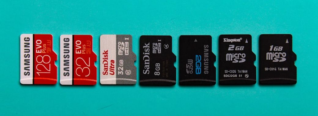 The image features several microSD cards arranged in a row on a turquoise background. The cards are from different brands including Samsung and SanDisk, showcasing their storage capacities. — Credit: Photo by Supratik Deshmukh on Unsplash