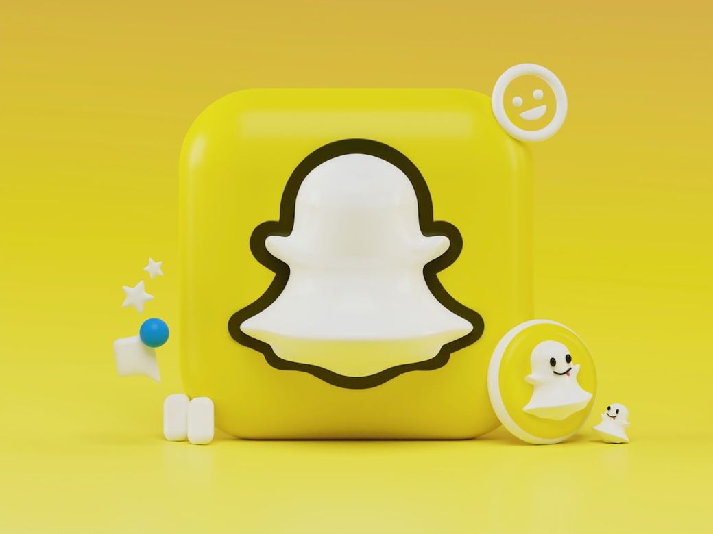 The image features a stylized representation of the Snapchat logo against a bright yellow background. Accompanying the logo are various playful elements, including smiley faces and stars, enhancing its vibrant and youthful appeal. — Credit: Photo by Alexander Shatov on Unsplash