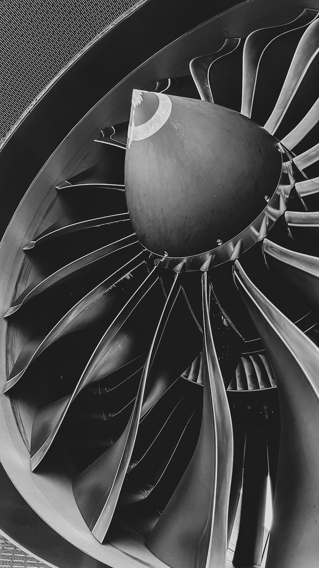 The image showcases a close-up view of an aircraft engine's turbine, highlighting the intricate design of the fan blades and the central cone. The monochrome color scheme emphasizes the engineering details and textures of the components. — Credit: Photo by Javier Vermaas on Unsplash
