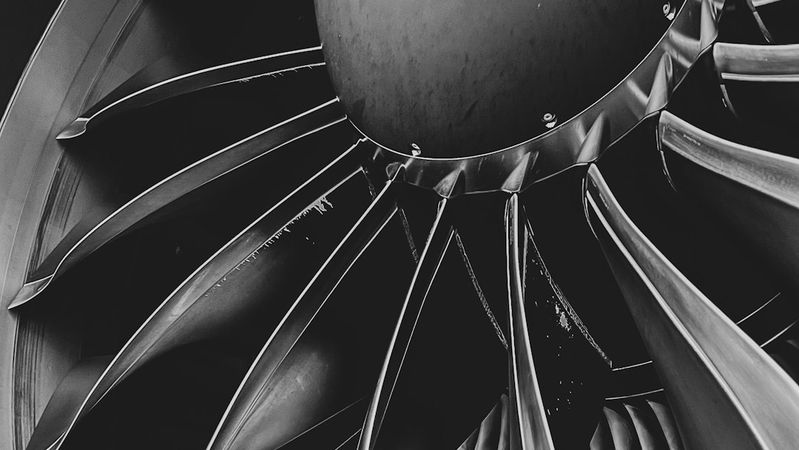 The image showcases a close-up view of an aircraft engine's turbine, highlighting the intricate design of the fan blades and the central cone. The monochrome color scheme emphasizes the engineering details and textures of the components.