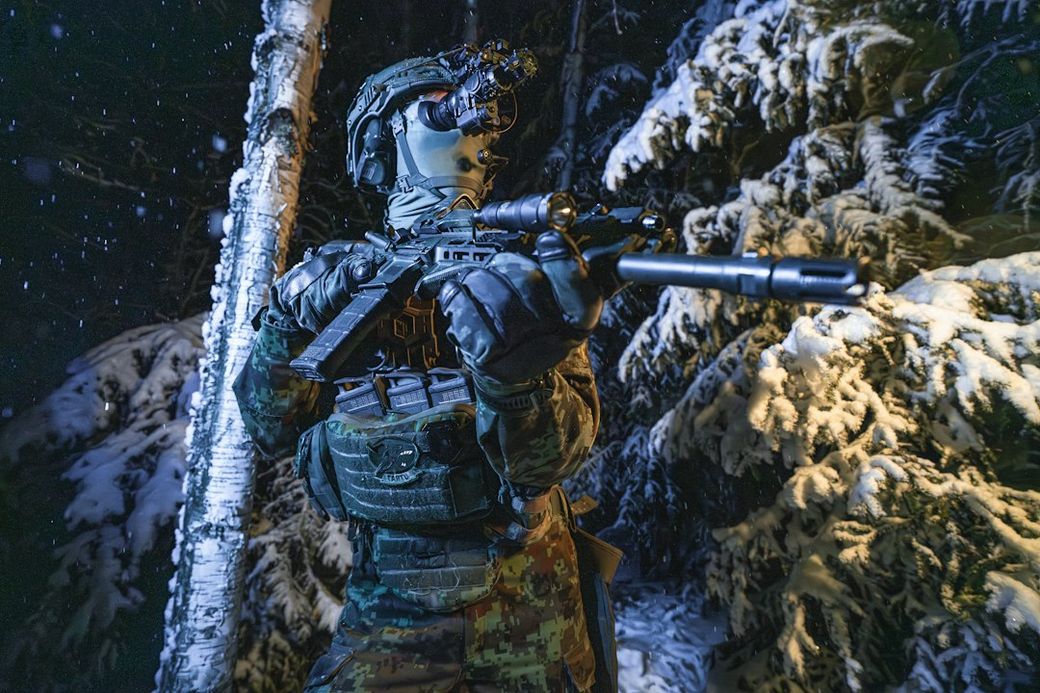 A soldier equipped with tactical gear stands in a snowy forest at night, holding a firearm and scanning the surroundings. The scene captures the soldier's focused expression and the dramatic contrast of the dark foliage against the bright snow. — Credit: Photo by Jaanus Jagomägi on Unsplash