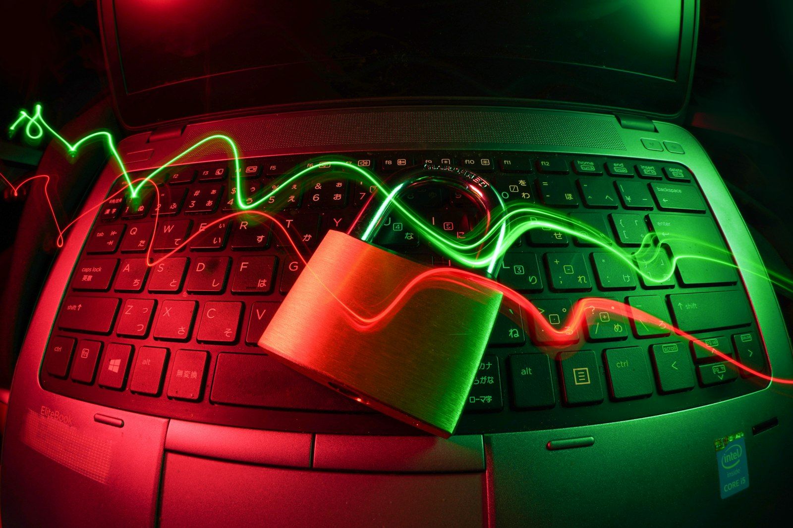 The image showcases a laptop keyboard with a metallic padlock placed on it, illuminated by red and green light trails. The contrasting colors and lighting create a sense of digital security and technology.