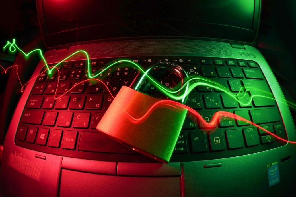 The image showcases a laptop keyboard with a metallic padlock placed on it, illuminated by red and green light trails. The contrasting colors and lighting create a sense of digital security and technology. — Credit: Photo by FlyD / Unsplash