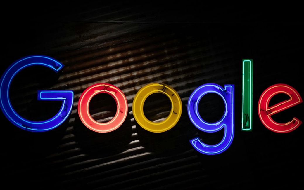 The image features the colorful neon sign of Google displayed prominently against a dark background. The letters are illuminated, showcasing the company's iconic branding. — Credit: Photo by Mitchell Luo / Unsplash