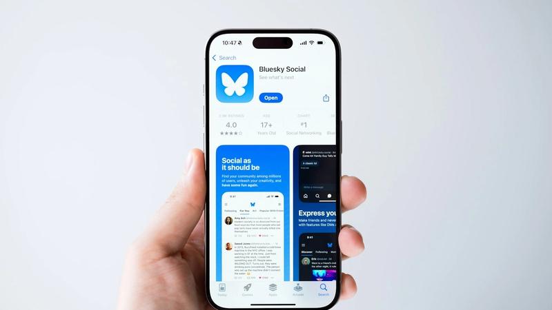 The image shows a hand holding a smartphone displaying the Bluesky Social app on its screen. The app's interface includes user reviews and features designed for social networking.