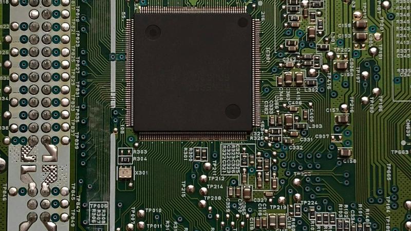 The image features a close-up view of a circuit board, showcasing various electronic components and intricate pathways. The central focus is on two prominent black chips with engraved text surrounded by smaller circuitry elements.