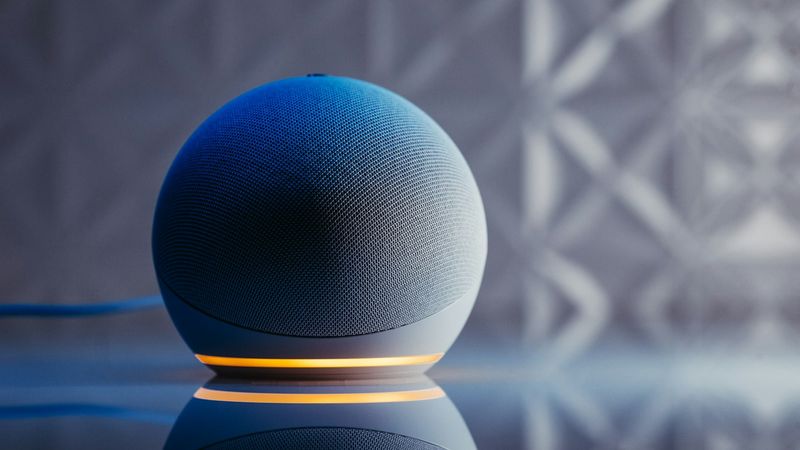 The image features a modern smart speaker with a spherical design, illuminated by a soft orange light. The sleek surface reflects the speaker's design against a textured background.
