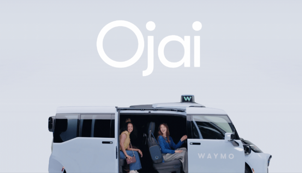 The image features two women seated inside a modern autonomous vehicle by Waymo. The background displays the word 'Ojai' prominently above the vehicle.