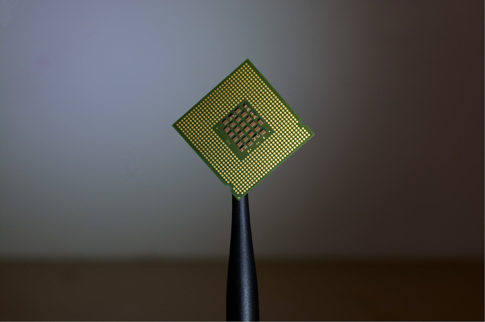 The image shows a close-up view of a computer processor held by a tool, highlighting the intricate design and structure of the microchip. The background is softly blurred, emphasizing the processor's details.