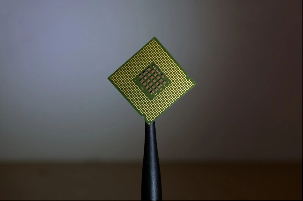 The image features a close-up of a microprocessor chip held by tweezers. The chip is shown against a neutral background, illustrating its intricate design and structure. — Credit: Photo by Brian Kostiuk / Unsplash