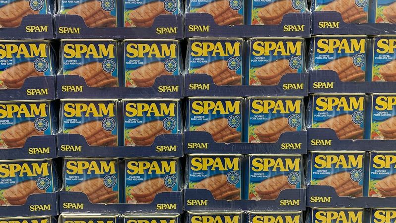An organized display of canned Spam products stacked on shelves. The packaging features bright colors and clear branding, emphasizing the product's presence in a retail environment.