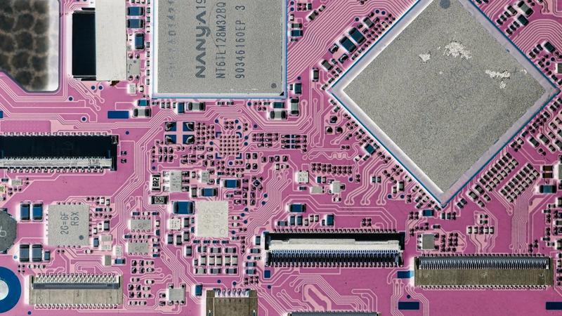 The image displays a close-up view of a pink circuit board, featuring various electronic components such as microchips and capacitors. The intricate patterns and connections are indicative of advanced technology in electronics.