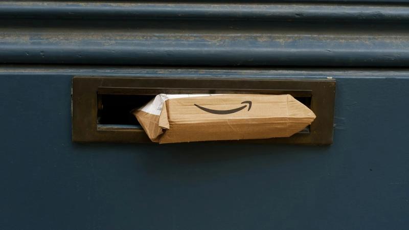 A cardboard package featuring the Amazon logo is partially inserted into a mailbox with a dark blue exterior. The image captures the delivery of goods directly to a home or office setting.