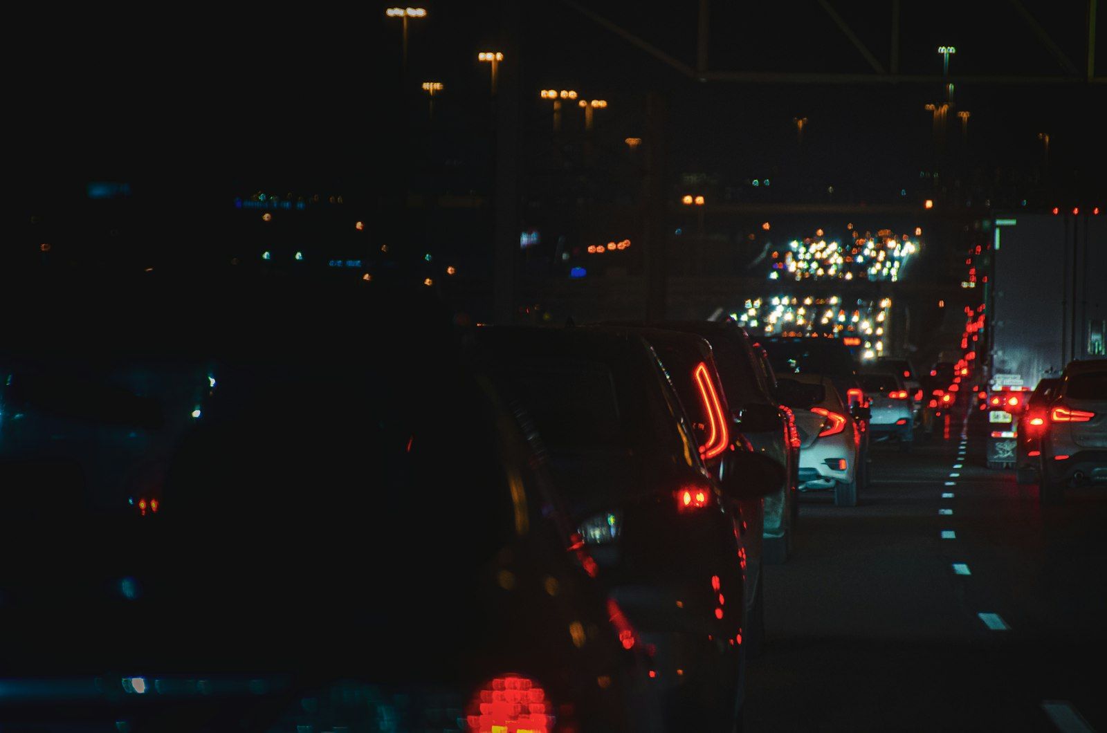 The image shows a congested highway at night, with a line of cars illuminated by their tail lights. The background is a blur of colorful traffic lights, indicating a heavy flow of vehicles.