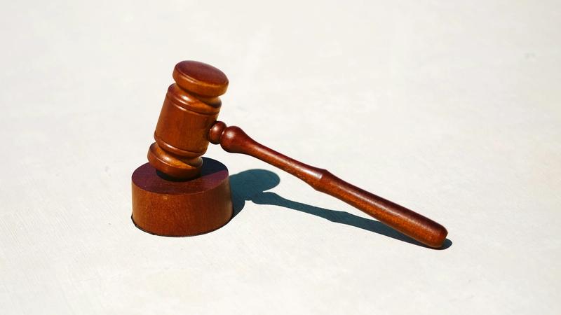 The image features a wooden gavel leaning against its base on a light-colored surface. This symbolizes authority in a legal context and is commonly associated with court proceedings.