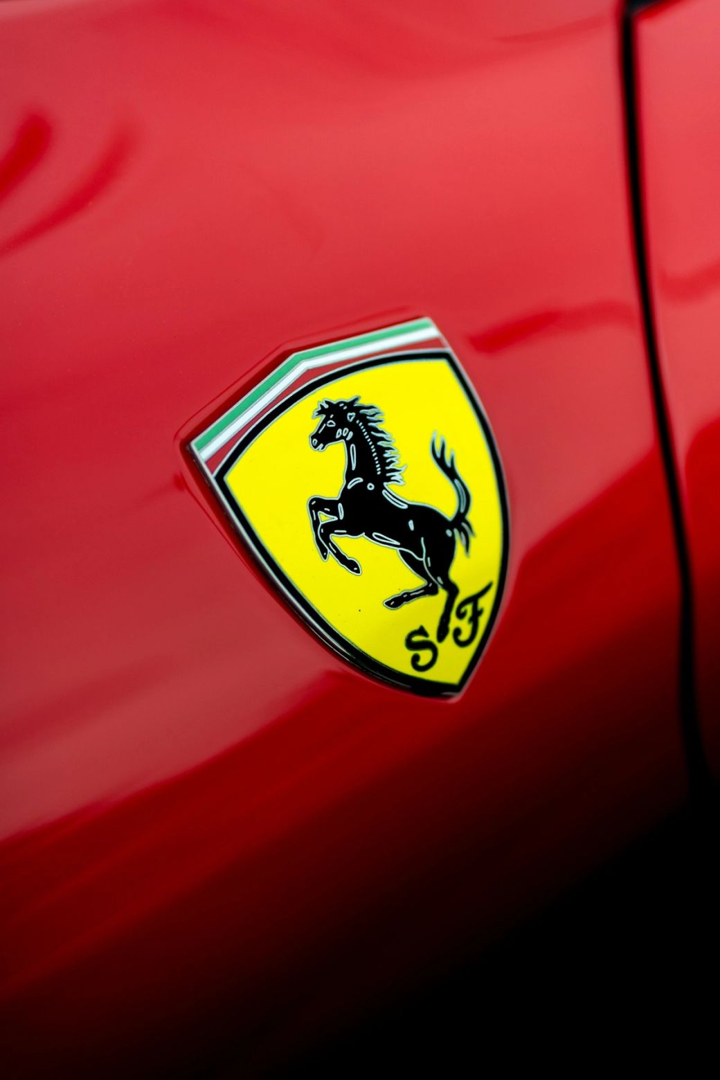 The image features a close-up of the Ferrari logo, prominently displayed on a red background. The logo showcases a black stallion rearing up against a yellow shield, emphasizing luxury and performance. — Credit: Photo by Krzysztof Hepner / Unsplash