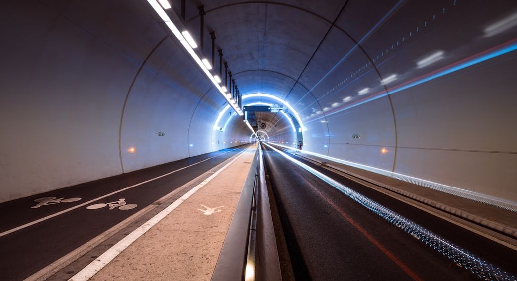 The image depicts a tunnel illuminated with bright lights, creating a dynamic visual effect. The dual lanes show a clear division for vehicles and a bike lane, suggesting a designed infrastructure for both motorists and cyclists. — Credit: Photo by Hugues de BUYER-MIMEURE on Unsplash