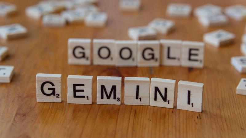 The image features wooden letter tiles arranged to spell out the words 'GOOGLE' and 'GEMINI' on a wooden surface. The composition highlights the playful and creative use of letter tiles, commonly associated with word games.