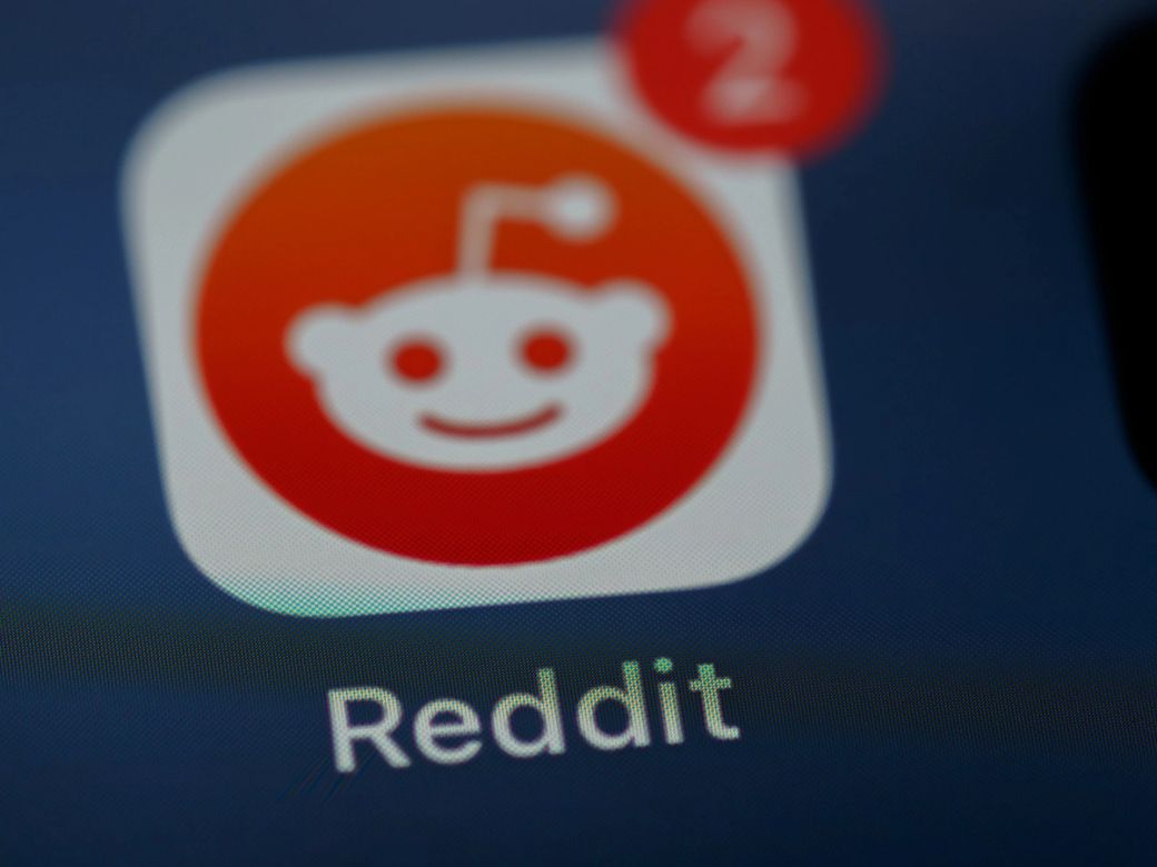 The image features a close-up view of the Reddit app icon, showcasing its distinct logo with a smiling mascot against a gradient background. A notification bubble is visible, indicating two unread messages. — Credit: Photo by Brett Jordan / Unsplash