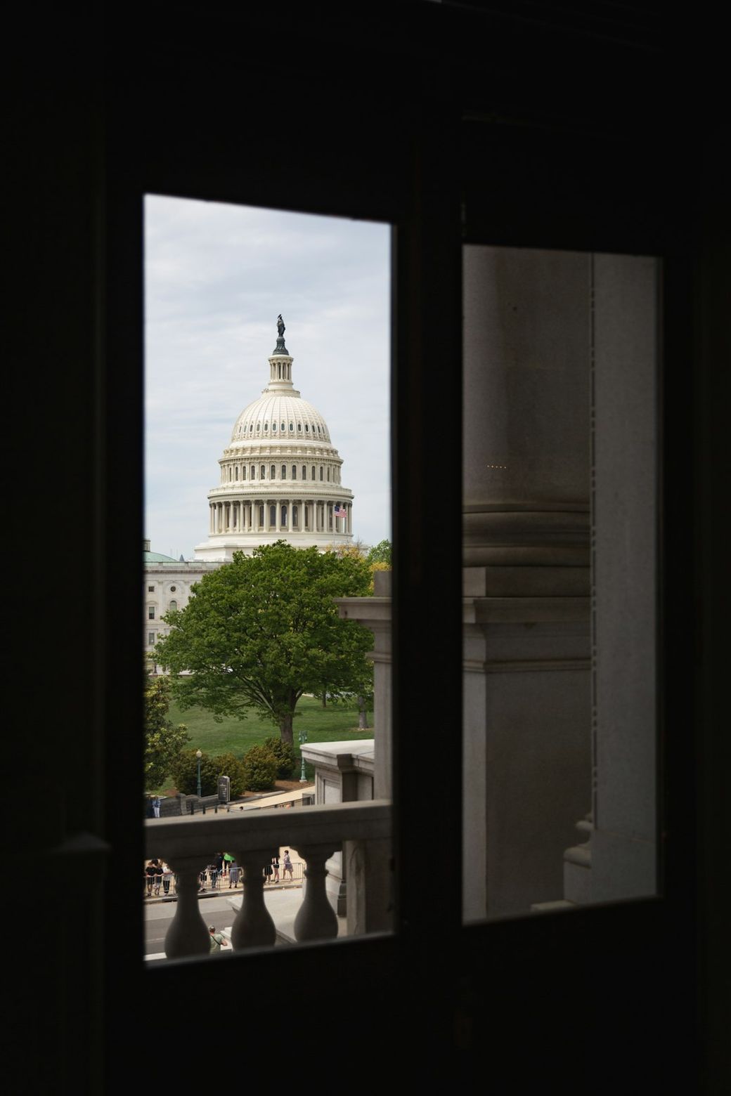 The image captures the United States Capitol building as seen through a doorway. The view highlights the iconic dome and surrounding greenery, framing the structure amidst a partially shaded setting. — Credit: Photo by Benjamin Ashton on Unsplash