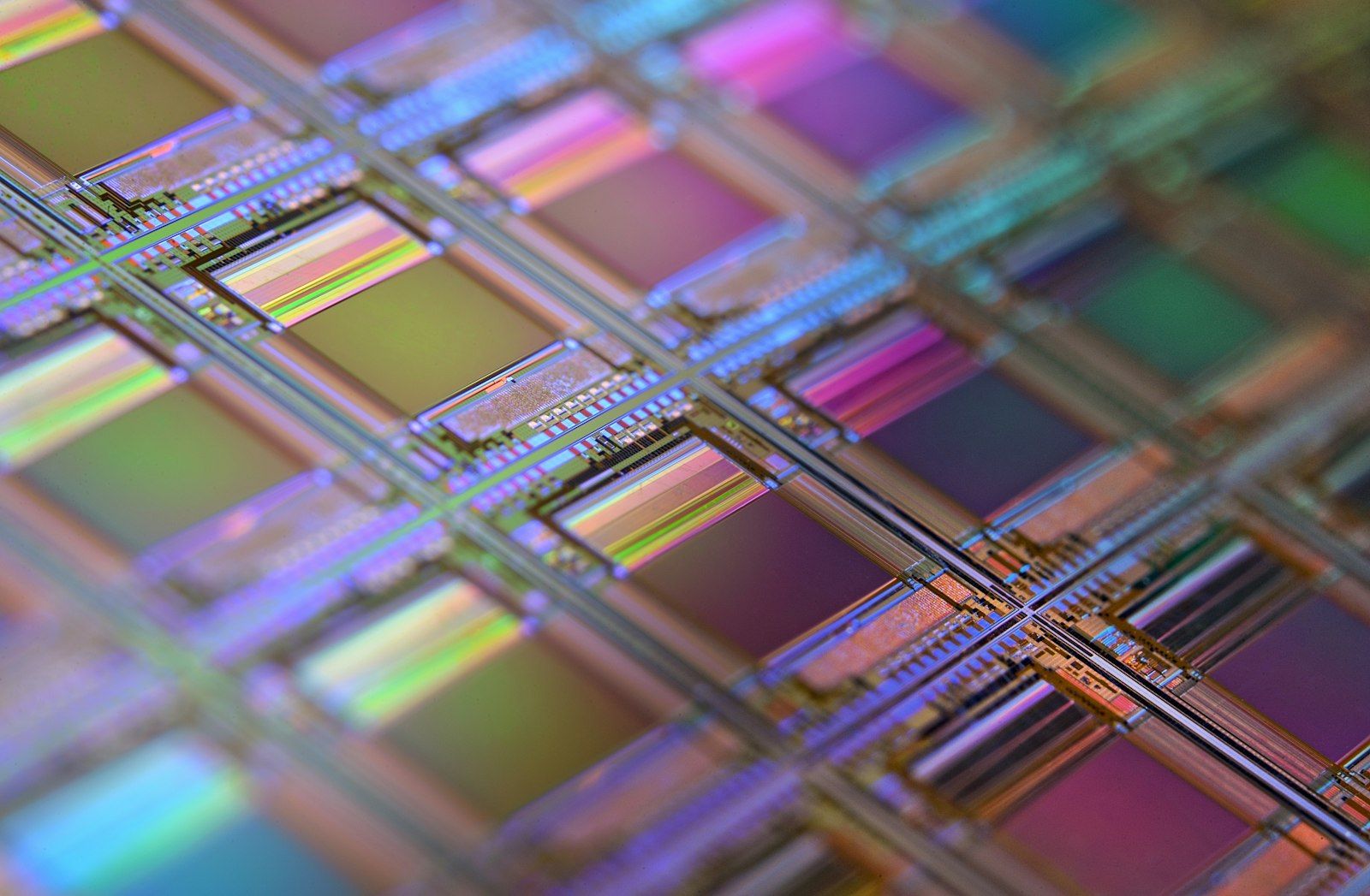 The image showcases a close-up view of a silicon wafer, characterized by its intricate, reflective microchip patterns. This high-tech surface exhibits a vibrant spectrum of colors due to the light interference in its layers.