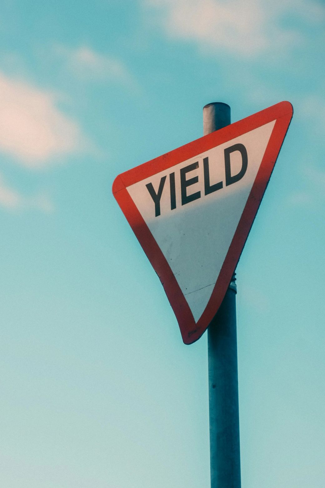 A close-up image of a yield traffic sign against a clear blue sky. The sign is prominently displayed, featuring a red triangle shape with the word 'YIELD' in bold black letters. — Credit: Photo by Ibrahim guetar / Unsplash