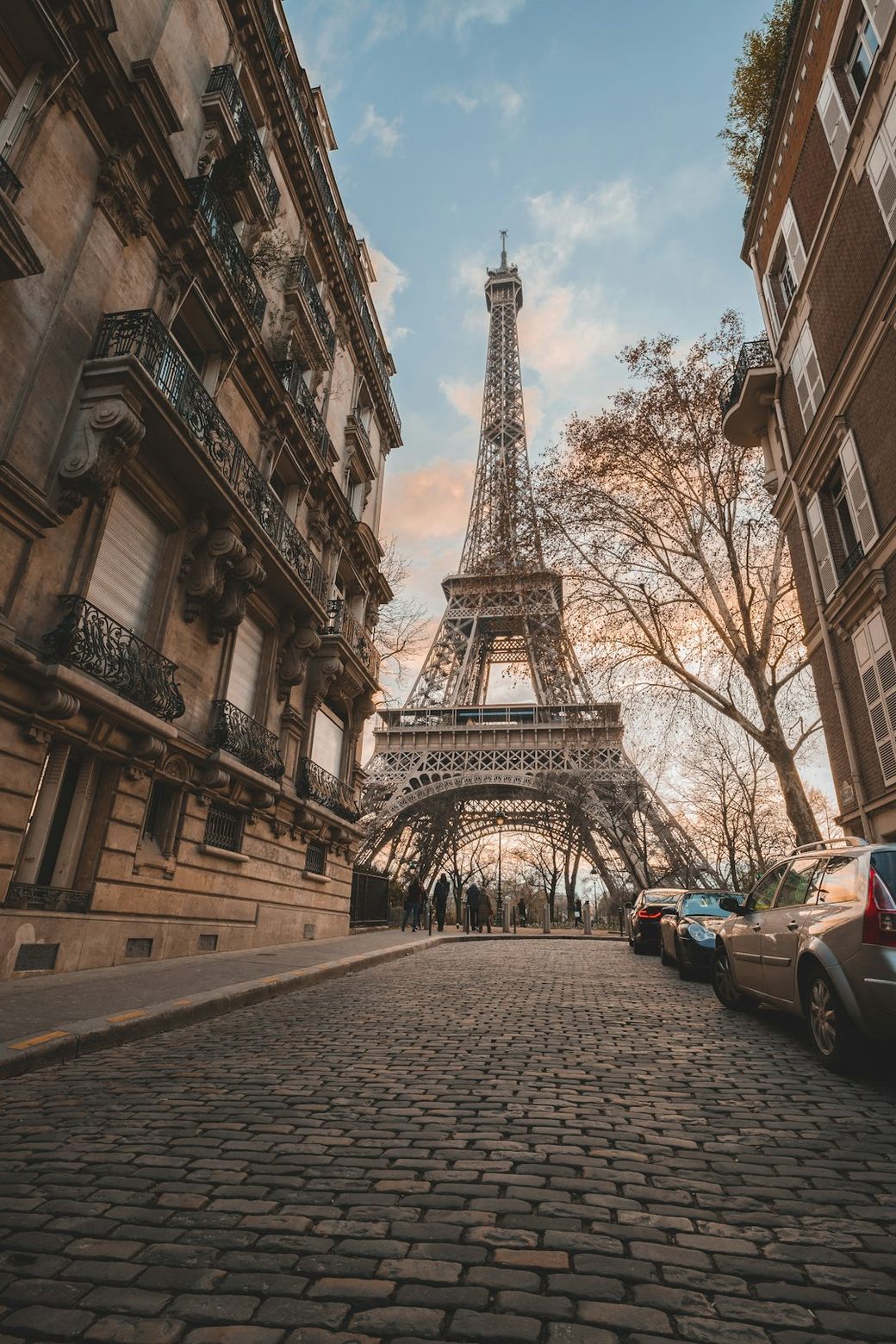 The image captures the iconic Eiffel Tower in Paris, framed by cobblestone streets and historical architecture. The tower is bathed in soft light during the golden hour, creating a picturesque urban scene. — Credit: Photo by cyril mzn on Unsplash