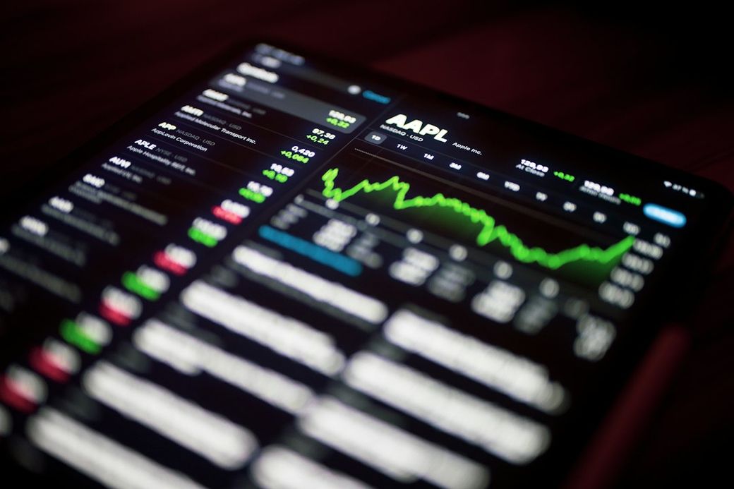 The image shows a close-up of a tablet screen displaying stock market data, with an emphasis on the stock performance of Apple Inc. (AAPL). Various stock prices and charts are visible, indicating active trading activity. — Credit: Photo by Dimitri Karastelev on Unsplash