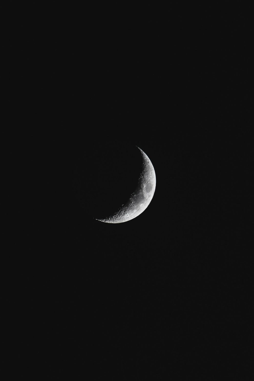A close-up view of a crescent moon against a dark background, showcasing its illuminated and shadowed features. The image captures the delicate curvature and surface details of the lunar surface. — Credit: Photo by Luke Stackpoole / Unsplash