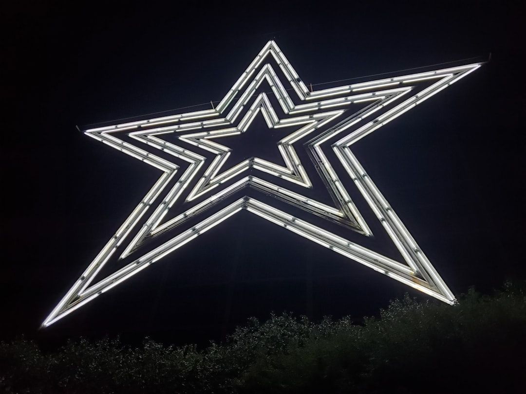 The image features a large illuminated star sculpture against a dark night background. The star is composed of glowing neon lights, creating a striking visual effect.