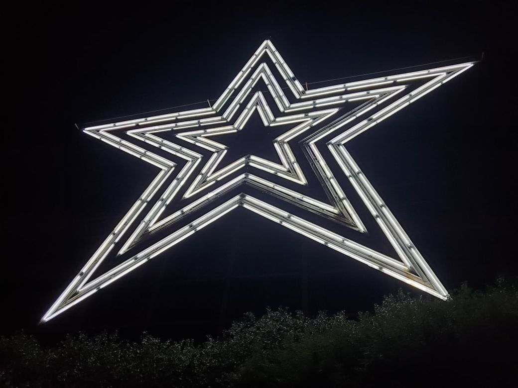 The image features a large illuminated star sculpture against a dark night background. The star is composed of glowing neon lights, creating a striking visual effect. — Credit: Photo by B R on Unsplash