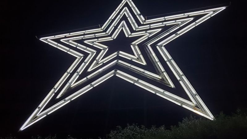 The image features a large illuminated star sculpture against a dark night background. The star is composed of glowing neon lights, creating a striking visual effect.