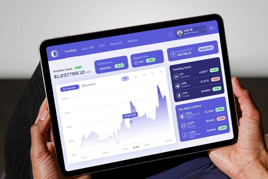 The image shows a person holding a tablet displaying a stock trading interface. The dashboard features financial data, including portfolio value and trending gains of various stocks. — Credit: Photo by Coinstash Australia / Unsplash