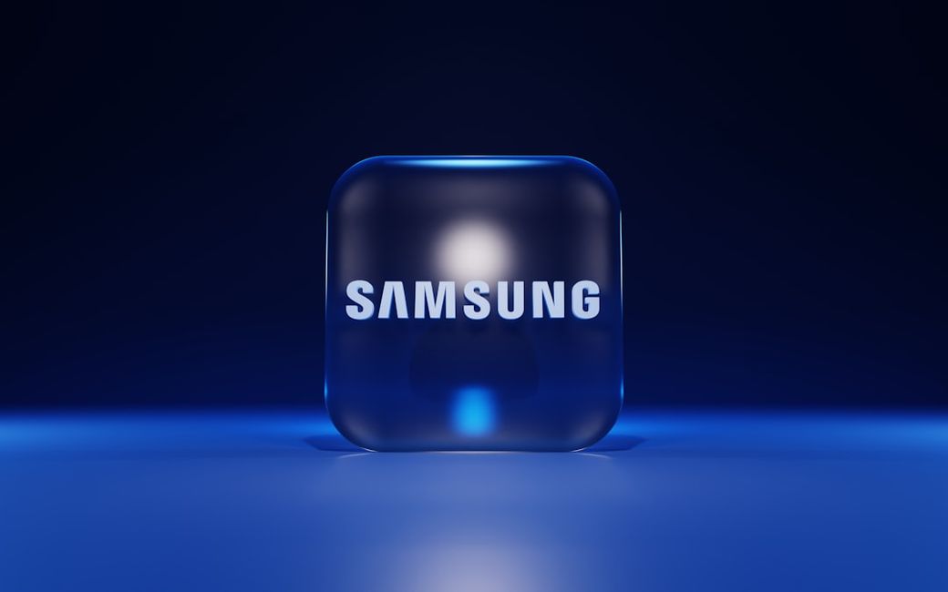 The image features a three-dimensional, illuminated cube with the Samsung logo prominently displayed on it. The background is a deep blue, creating a modern and tech-focused aesthetic. — Credit: Photo by BoliviaInteligente on Unsplash