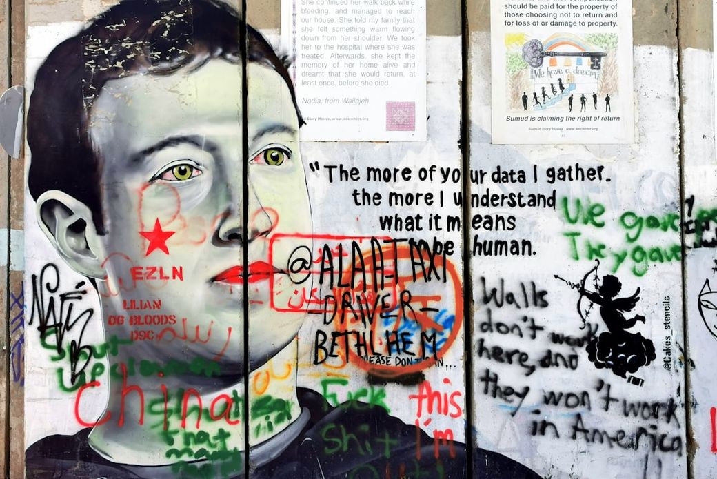 The image features a mural of a man with a serious expression, surrounded by various graffiti texts and symbols on a wall. The artwork appears to critique technology and data privacy, with phrases expressing strong opinions on personal data and surveillance. — Credit: Photo by Snowscat on Unsplash
